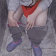 A long-haired girl in gray sweatpants sits on a toilet, viewed from the front. Poop action is visible from a between the legs perspective. She tears off toilet paper again and again, wiping her ass several times. Vertical format video. Over 3 minutes.